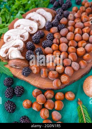 Gesunde Herbstgerichte: Weiße Champignons, geschälte Haselnüsse, Rucola-Rucola-Salat, Brombeeren und kleiner Tannenzweig auf grünem Hintergrund. Stockfoto