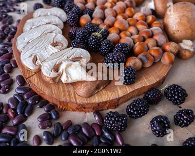 Gesunde Herbstgerichte: Weiße Champignons, geschälte Haselnüsse, violette Nierenbohnen, Brombeeren und kleine Tannenzweigen auf einer Holzscheibe. Stockfoto