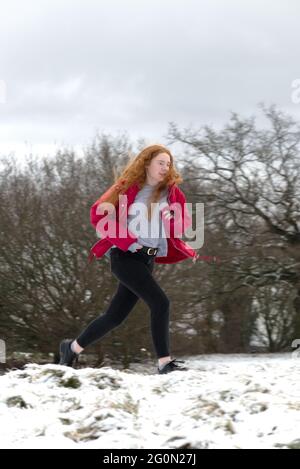 Rote Haare Mädchen in rotem Mantel läuft in den verschneiten Wäldern Stockfoto