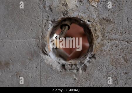 Blick auf das Loch in der Wand, wo der Handwerker die Drähte repariert, die sie schneiden. Stockfoto