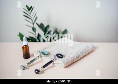 Jade guasha Massagerollen auf dem Handtuch und Serumflasche, SPA Relax, Gesichts- und Hautpflegekonzept Stockfoto