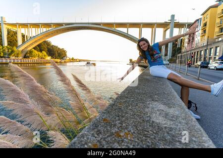 Junge schöne Frau, die für ein Foto vor der Arrabida-Bogenbrücke in Porto, Portugal posiert Stockfoto