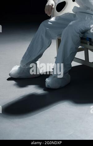 Auf dem Bett sitzend, sind die Beine der jungen Ärzte erschöpft Stockfoto