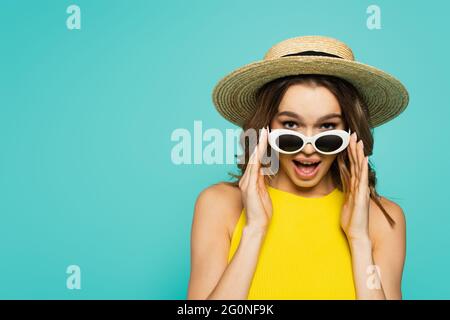 Aufgeregt Frau in Strohhut mit Sonnenbrille isoliert auf blau Stockfoto