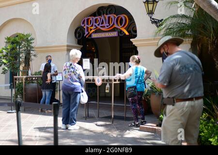 Menschen mit Gesichtsmasken stehen vor dem Prado Restaurant und warten auf einen Tisch während der frühen Tage nach dem Aufstehen im Blboa Park, San Diego, CA Stockfoto