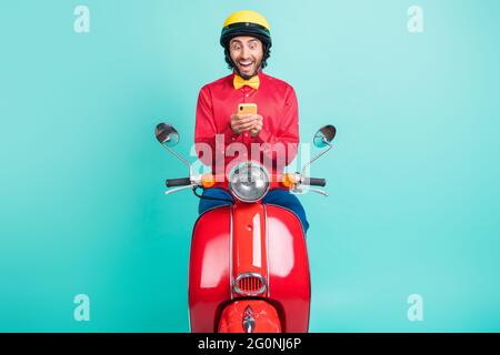 Foto von beeindruckt Brünette Kerl Fahrt auf Fahrrad halten Telefon tragen rotes Hemd Helm isoliert auf teal Farbe Hintergrund Stockfoto