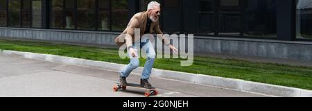 Voller glücklicher Mann mittleren Alters in Sonnenbrillen, der draußen auf Longboard reitet, Banner Stockfoto