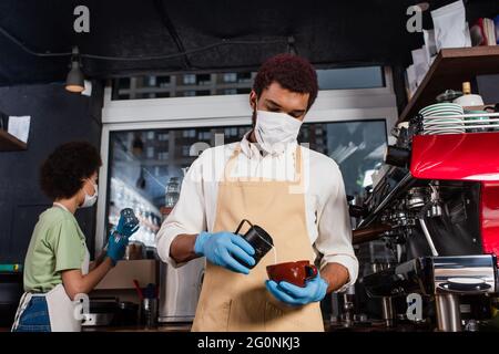 afroamerikanischer Barista in medizinischer Maske, der Kaffee im Café zubereitet Stockfoto