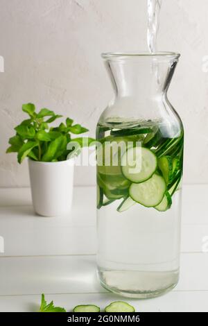 Wasser wird in die Kanne gegossen. Frisches Wasser mit Gurken und Minze Zweige, Detox Getränk infundiert. Gesundheit, Fitness, gesunde Ernährung Konzept. Stockfoto