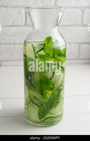 Wasser wird in die Kanne gegossen. Frisches Wasser mit Gurken und Minze Zweige, Detox Getränk infundiert. Gesundheit, Fitness, gesunde Ernährung Konzept. Stockfoto