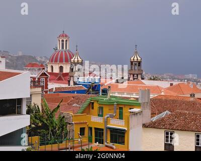 Blick über die roten Ziegeldächer und die drei sehr unterschiedlichen Kirchtürme aus der Stadt La Orotava im Norden der Insel Teneriffa. Blassblau Stockfoto