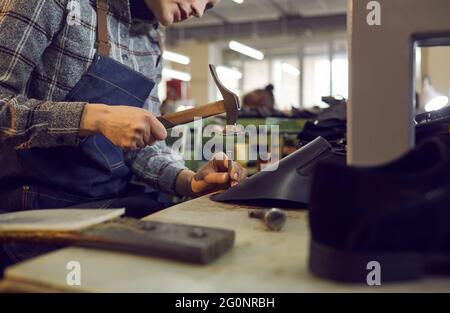 Schuhfabrikarbeiter sitzt am Tisch und verwendet professionelle Werkzeuge, um Lederstiefel zu machen Stockfoto