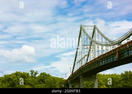 Eine moderne Fußgängerbrücke aus Eisen mit Kabelgefüge und einer Laterne vor einem blau bewölkten Himmel am Sommertag. Blick von unten auf einen Hig Stockfoto