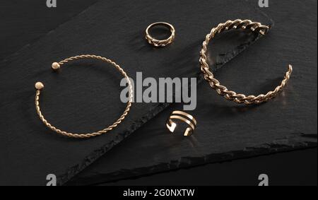 Modernes Design Goldene Armbänder und Ringe auf schwarzen Steintellern Stockfoto