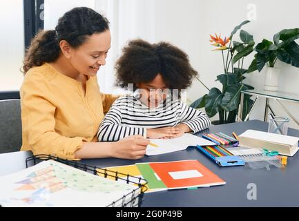 Mutter hilft ihrer Tochter, zu Hause Schulaufgaben zu machen. Glückliche Mutter und Schülerin, glückliche Familie Stockfoto