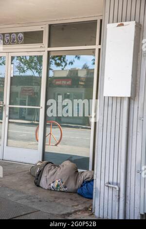 Obdachloser, der vor einem leeren Ladenlokal auf der Telegraph Ave. In Berkeley, Kalifornien, ein Nickerchen macht. Berkeley Peace Zeichen Fahrradständer im Fenster reflektiert für Stockfoto