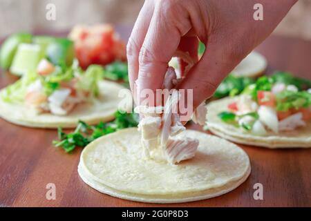 Hähnchenstücke auf einen kleinen Straßentaco auf ein Holzbrett legen. Stockfoto