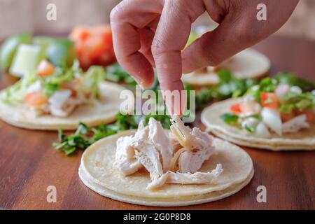 Hähnchenstücke auf einen kleinen Straßentaco auf ein Holzbrett legen. Stockfoto