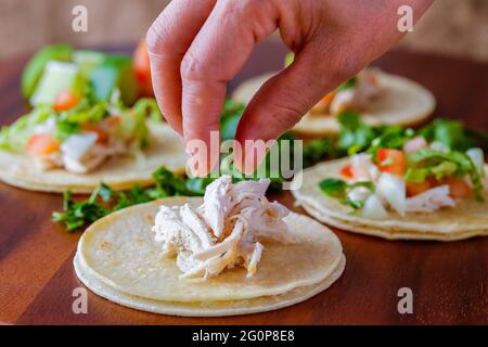 Hähnchenstücke auf einen kleinen Straßentaco auf ein Holzbrett legen. Stockfoto