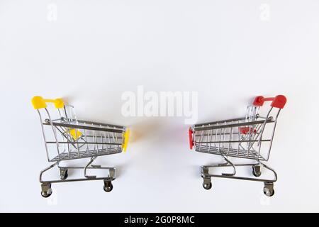 Zwei kleine leere dekorative Einkaufswagen mit gelben, roten Akzenten auf weißem Hintergrund, Platz für Text. Blick von oben. Mockup, Kopierbereich. Konzept b Stockfoto
