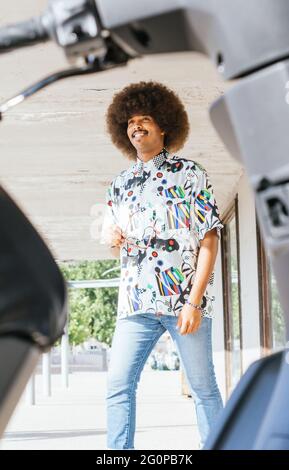 Junger schwarzer Kerl mit afro Haaren lächelnd Reiten mit unfokussierten Motorrad im Vordergrund Stockfoto