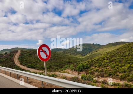 Schild „No Left Turn“ auf der Straße, umgeben von grünen Hügeln unter einem blau bewölkten Himmel Stockfoto