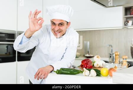 Männlicher Koch in weißer Uniform mit OK-Handzeichen an der Küche Stockfoto