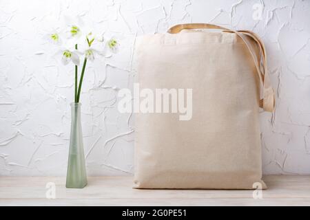 Canvas-Tragetasche Mockup mit weißen Lilien in der Glasvase. Rustikale Einkaufstasche aus Leinen für Branding-Präsentation Stockfoto