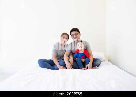 Vater, Mutter und Sohn aus Asien spielen auf dem Bett im Schlafzimmer Superhelden. Freundliche Familie, die Spaß hat Stockfoto