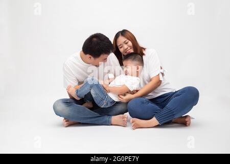 Fröhliche asiatische Familie sitzen über weißem Hintergrund haben Spaß Vater kitzeln kleinen Sohn. Junges Paar mit Kindern in weißem Oberteil und blauer Jeans. Pare Stockfoto