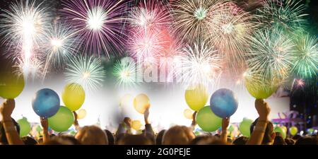 Abstrakt gefärbtes Feuerwerk am Nachthimmel und jubelnde Menge beim Neujahrsfest mit Ballon zur Hand Stockfoto