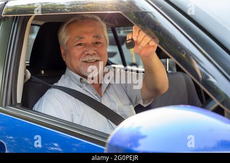 Asian Senior Mann Fahrer lächelnd und zeigt neue Autoschlüssel Und im Auto sitzen Stockfoto