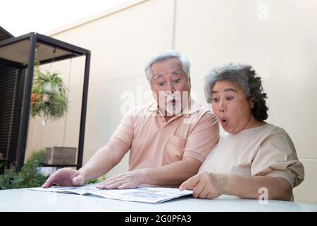 Aufgeregt asiatische ältere Paar Gefühl erstaunt durch gute Überraschung Nachrichten beim Lesen der Zeitung oder Zeitschrift im vorderen Garten zu Hause Stockfoto