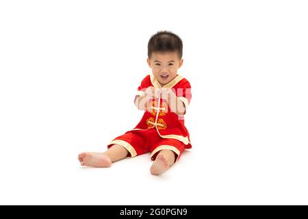 Asiatische baby boy sitzen und Show mini Herz mit Fingern und das Tragen der traditionellen Chinesischen Anzug auf weißem Hintergrund, verkleiden sich für Chinesischen neue Jahr f Stockfoto