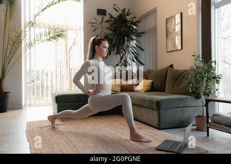 Gesundes Sport-Lifestyle-Konzept, glücklich lächelndes Mädchen, das Sport und Yoga-Übungen im Green Loft Innenhaus macht und Trainerübungen wiederholt Stockfoto