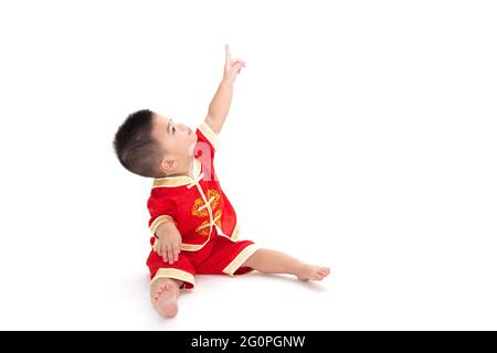 Asiatische baby boy sitzen und zeigen nach oben und das Tragen der traditionellen Chinesischen Anzug auf weißem Hintergrund, Dress up für Chinese New Year Festival conce Stockfoto