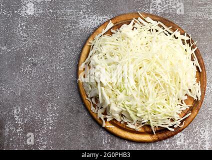 Weißkohl für Salat auf einem runden Holzbrett auf dunklem Hintergrund zerkleinert. Draufsicht, flach liegend Stockfoto