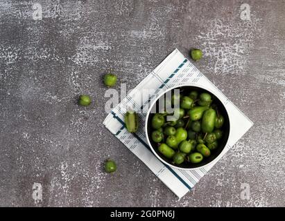 Mini-Kiwi-Babyfrucht (Actinidia arguta) in einer Schüssel auf dunklem Grund. Draufsicht, flach liegend Stockfoto