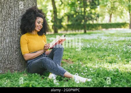Hübsche Afro-Frau, die in einem Garten ein Buch liest. Stockfoto