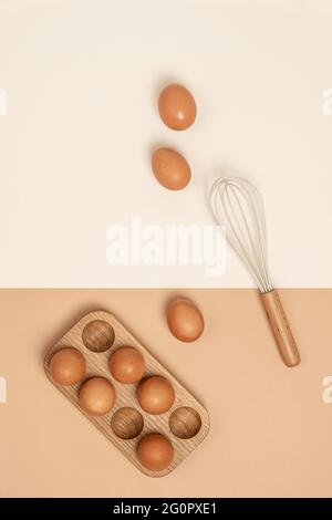 Eier in Holzeischachtel und Schneebesen auf beigem Hintergrund. Flach liegend Draufsicht Kopierbereich. Stockfoto