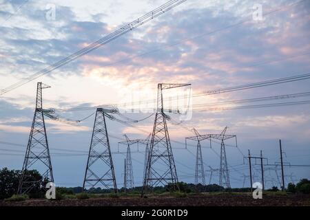 Elektrische Masten und Hochspannungsleitungen im Hintergrund bei Sonnenuntergang. Gruppieren Sie die Silhouette der Sendetürme. Stockfoto