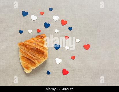 Ein typisch französisches frisches Croissant und Herzen in den Farben der französischen Flagge auf einer Leinentischdecke, Draufsicht, Bastille Day und French National Day c Stockfoto