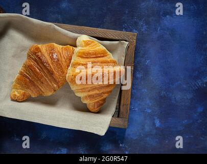 Frische französische Croissants in Holztablett auf blauem Hintergrund, Draufsicht Stockfoto