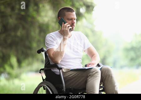 Behinderter Mann im Rollstuhl, der im Park auf dem Handy telefoniert Stockfoto