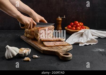 Weibliche Hand mit Messer geschnitten gekochten Rindfleisch Zungenrolle auf Holz Schneidebrett Stockfoto