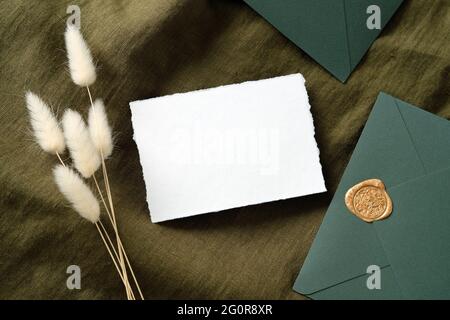 Rustikale Hochzeitspapierwaren, Draufsicht. Weißes Einladungskarten-Mockup, Umschläge, getrocknete Blumen auf grünem Stoff. Flach liegend, Draufsicht, Kopierbereich. Stockfoto