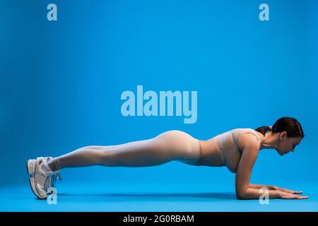 Frau, die auf blauem Hintergrund in der Plankenstellung des Unterarms steht Stockfoto
