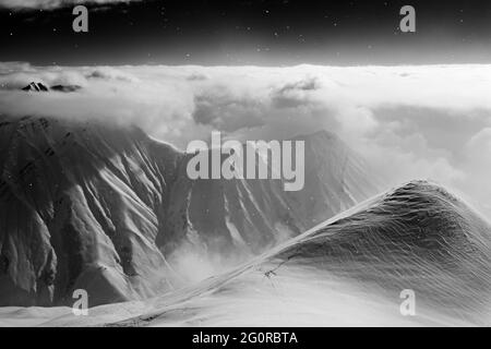 Schwarz-weiße, hoch verschneite Berge, bedeckt mit wunderschönen Wolken und Nebel bei Schneefall. Kaukasus-Berge in der Winternacht, Georgien, Region Gudauri. P Stockfoto