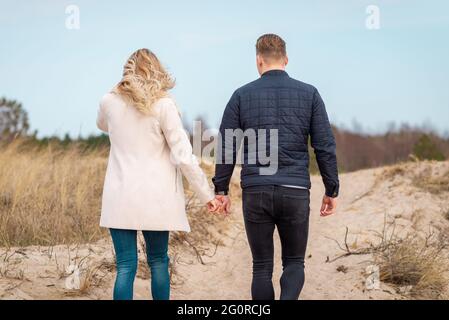 Ein junges Paar, das auf Sanddünen ging, hielt Hände.in der Ferne der Wald.Abenteuer Reise Lifestyle-Konzept. Stockfoto