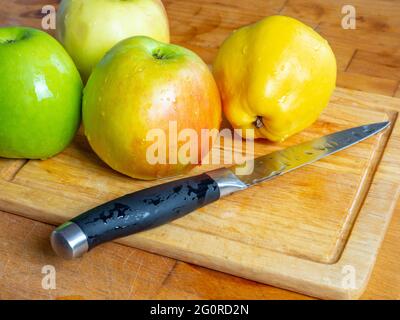 Messer, grüne Äpfel und gelbe Quitte mit Wassertropfen auf einem hölzernen Schneidebrett aus nächster Nähe. Speicherplatz kopieren. Stockfoto